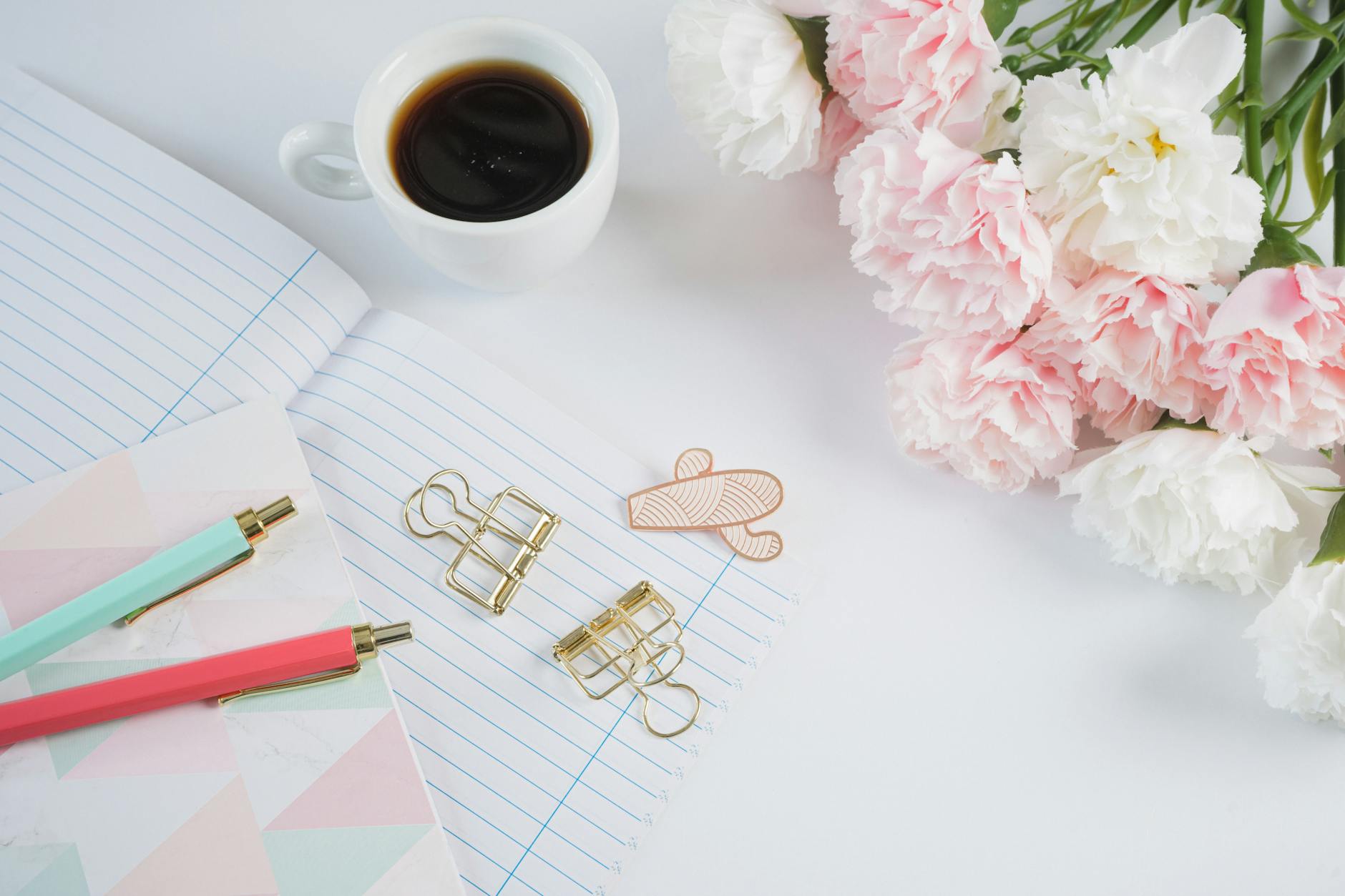 A stylish workspace with coffee, flowers, stationery, and notes.
