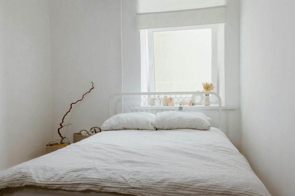 A serene white bedroom interior featuring a bed with pillows, natural light from