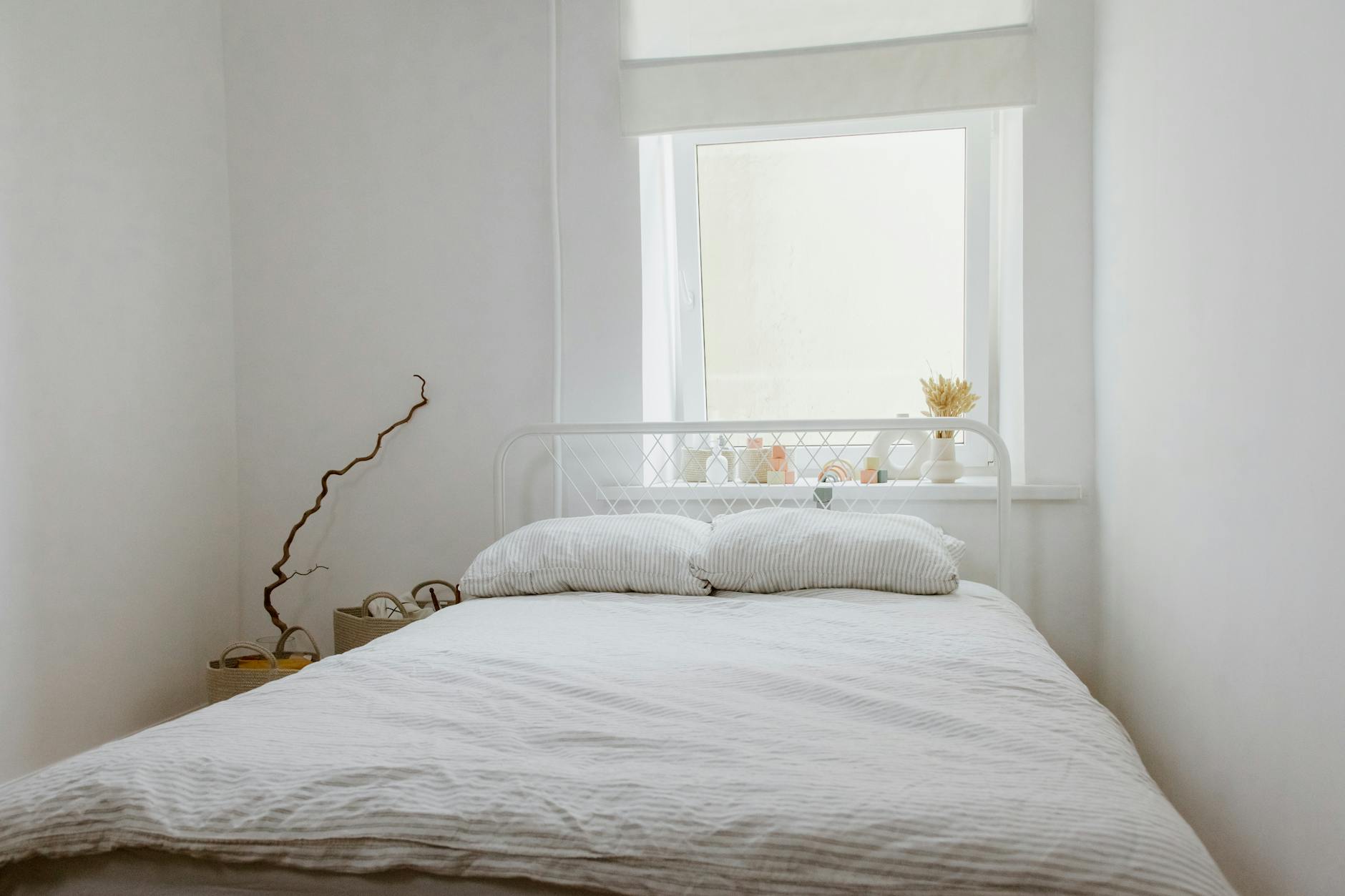 A serene white bedroom interior featuring a bed with pillows, natural light from