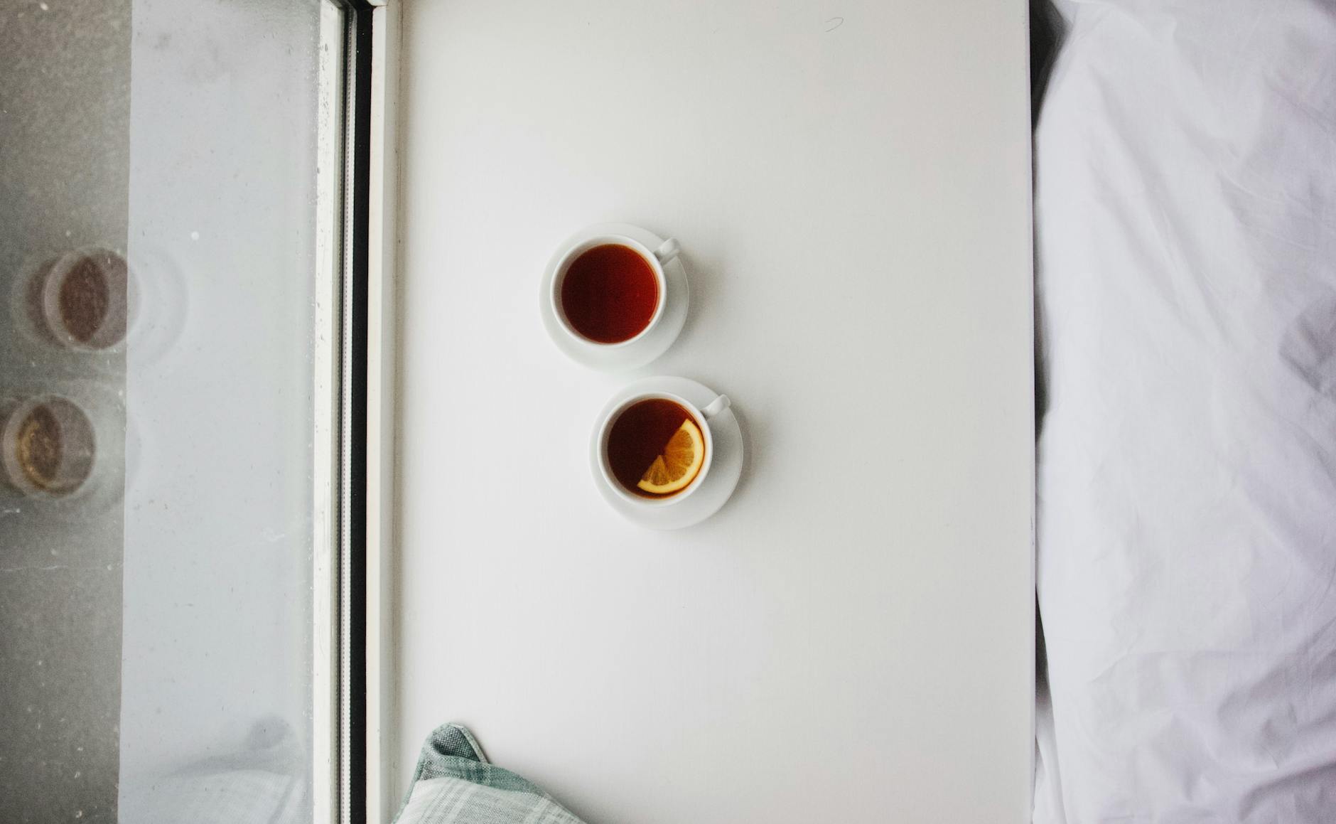 Top view of two cups of tea on a white table beside a window, creating a cozy at