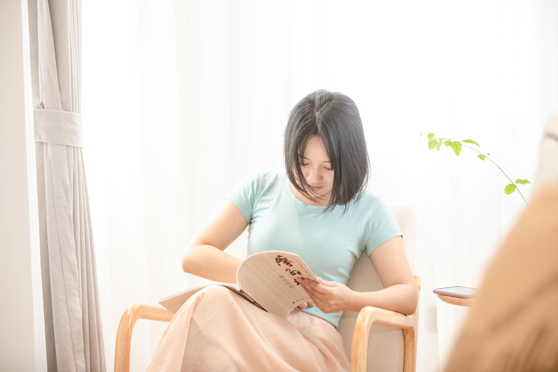 Asian woman relaxing and reading in a sunlit living room. Bright and peaceful at