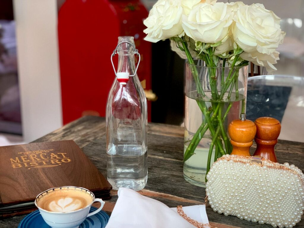 Chic café table arrangement featuring coffee, roses, and a pearl clutch on woode