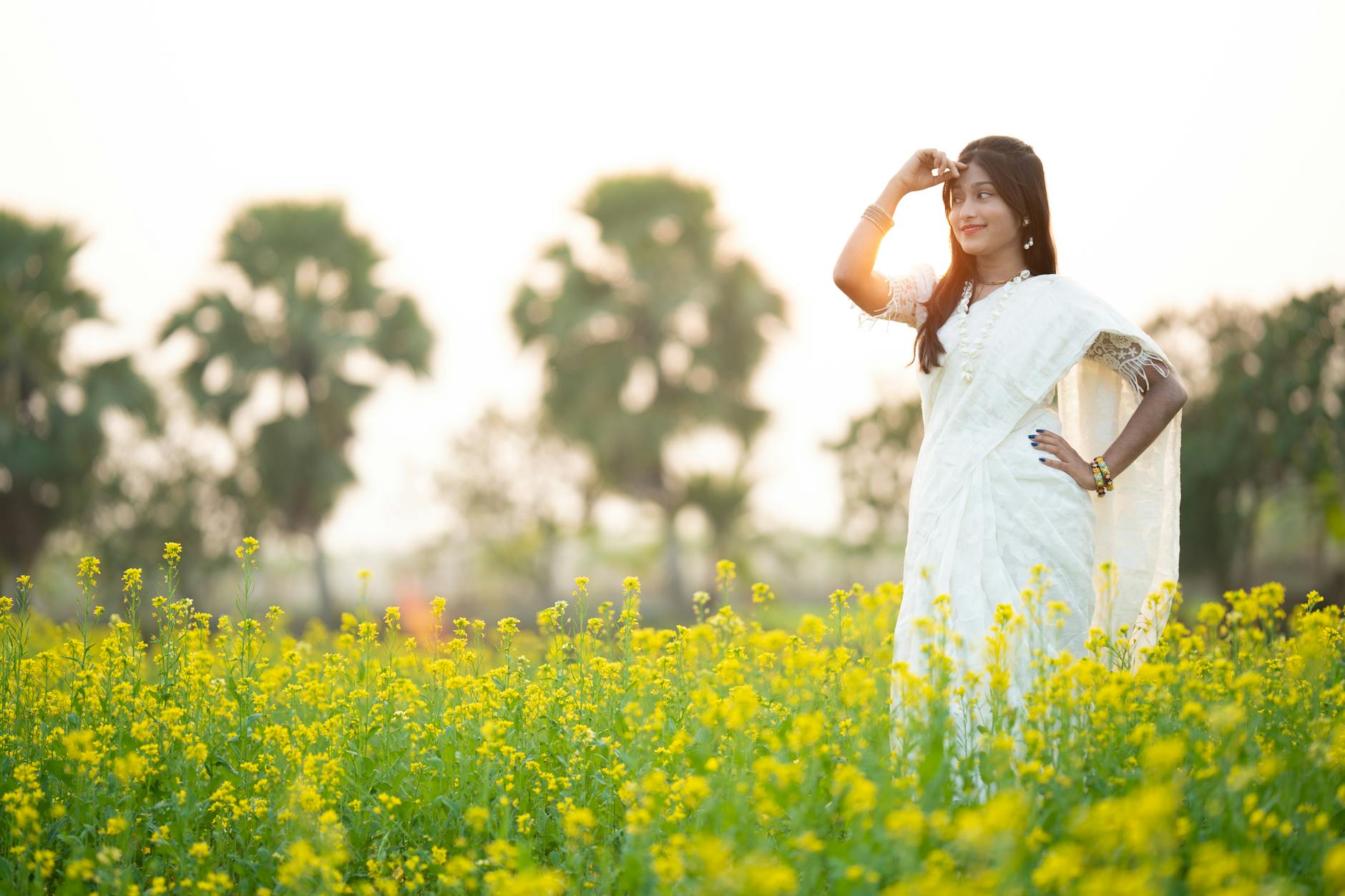 A woman in a white dress stands in a vibrant mustard field during the day.