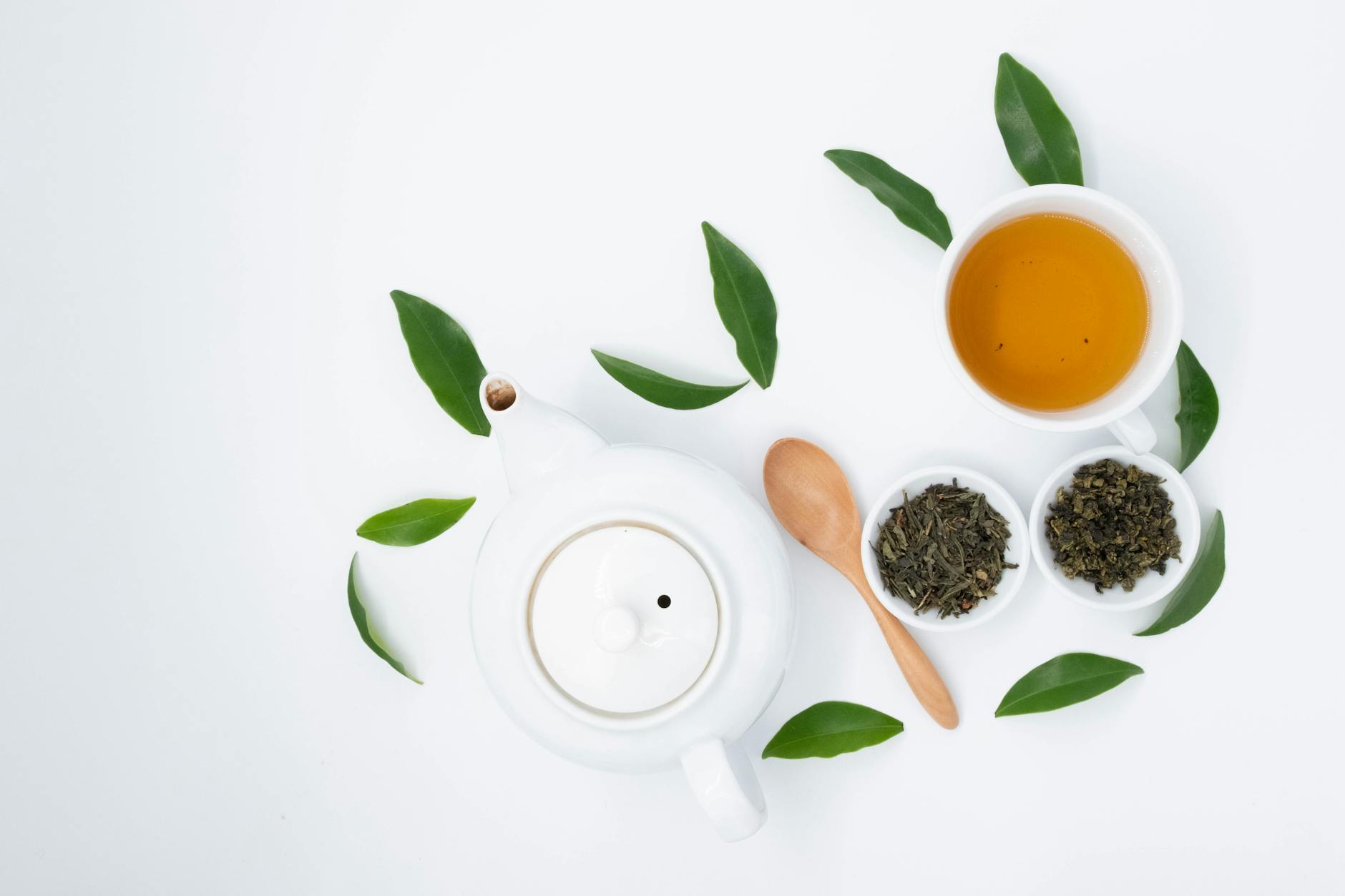 From above of cup with green tea near dry and fresh leaves with ceramic teapot o