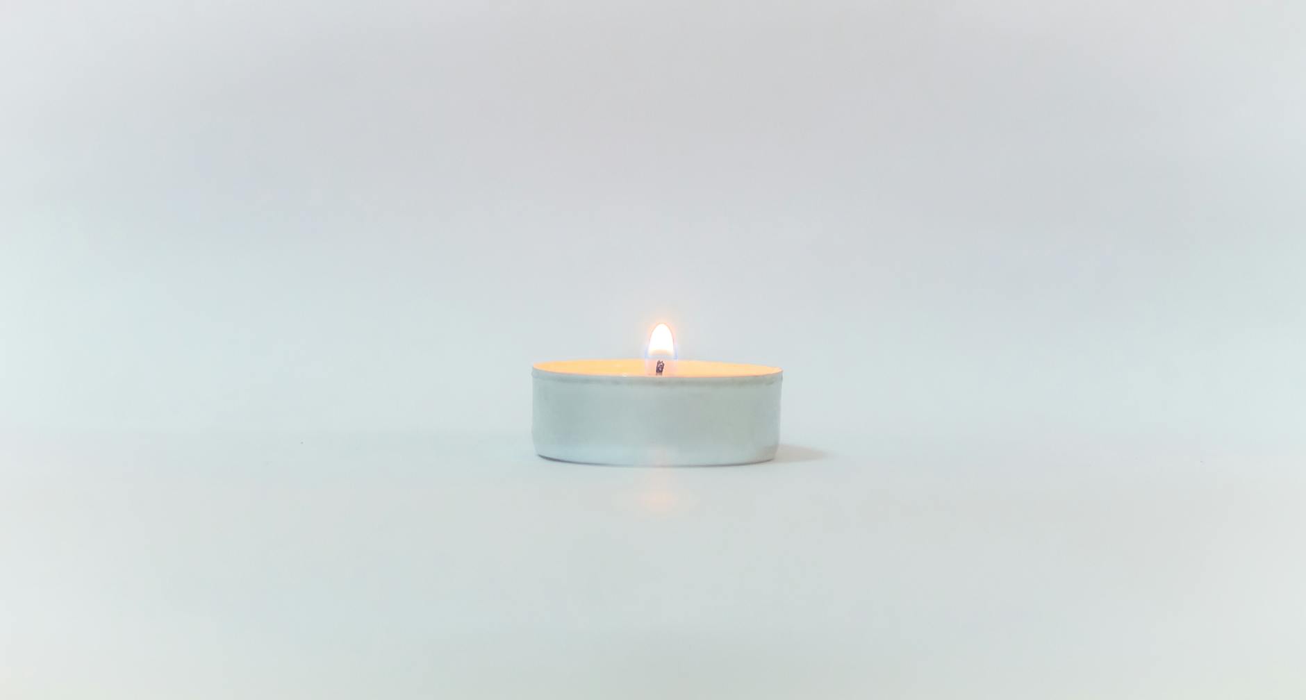 A minimalist white candle centered on a white background, featuring a small flam