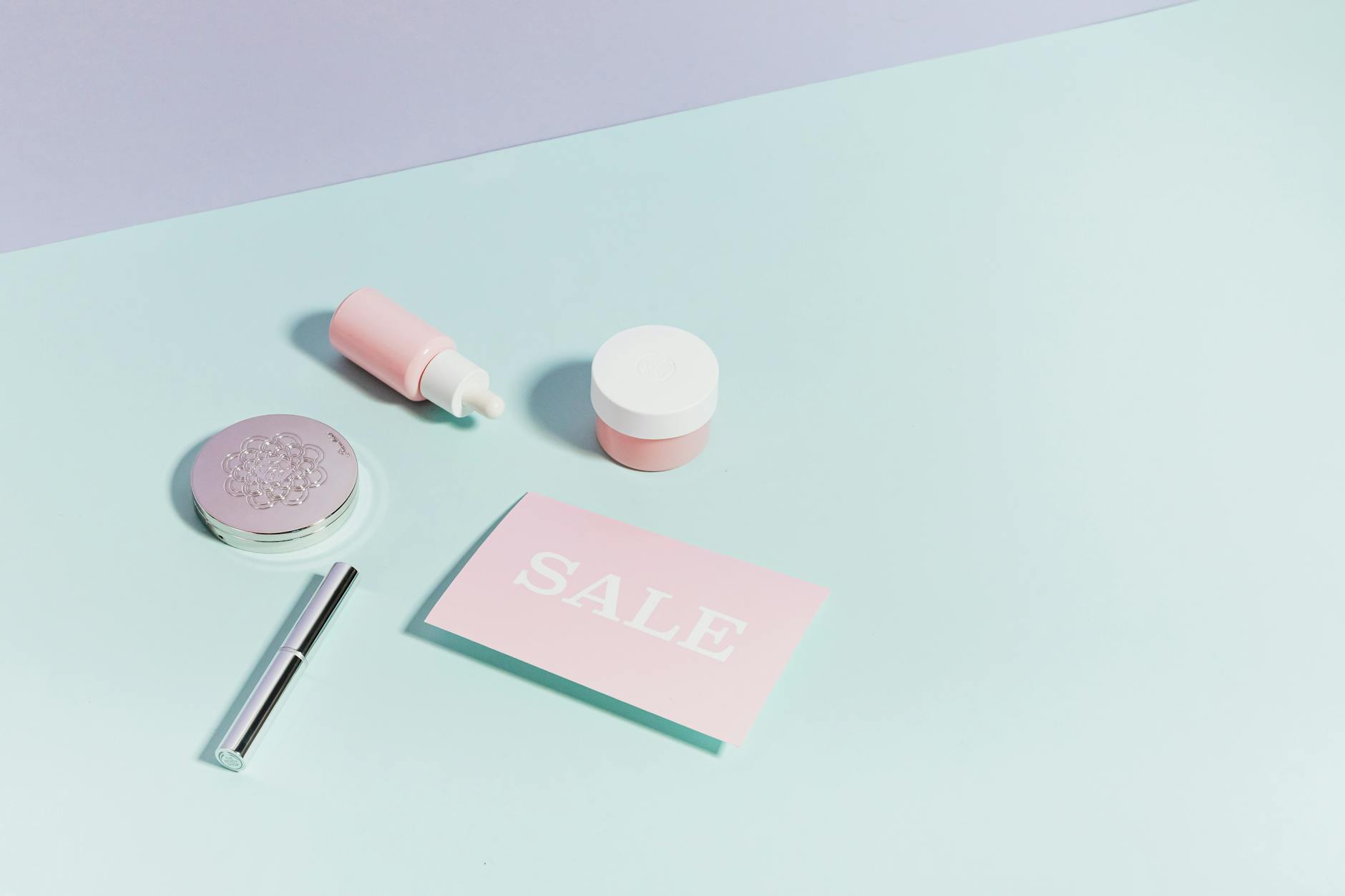 Clean flat lay of pastel pink beauty products and sale card on a light backgroun