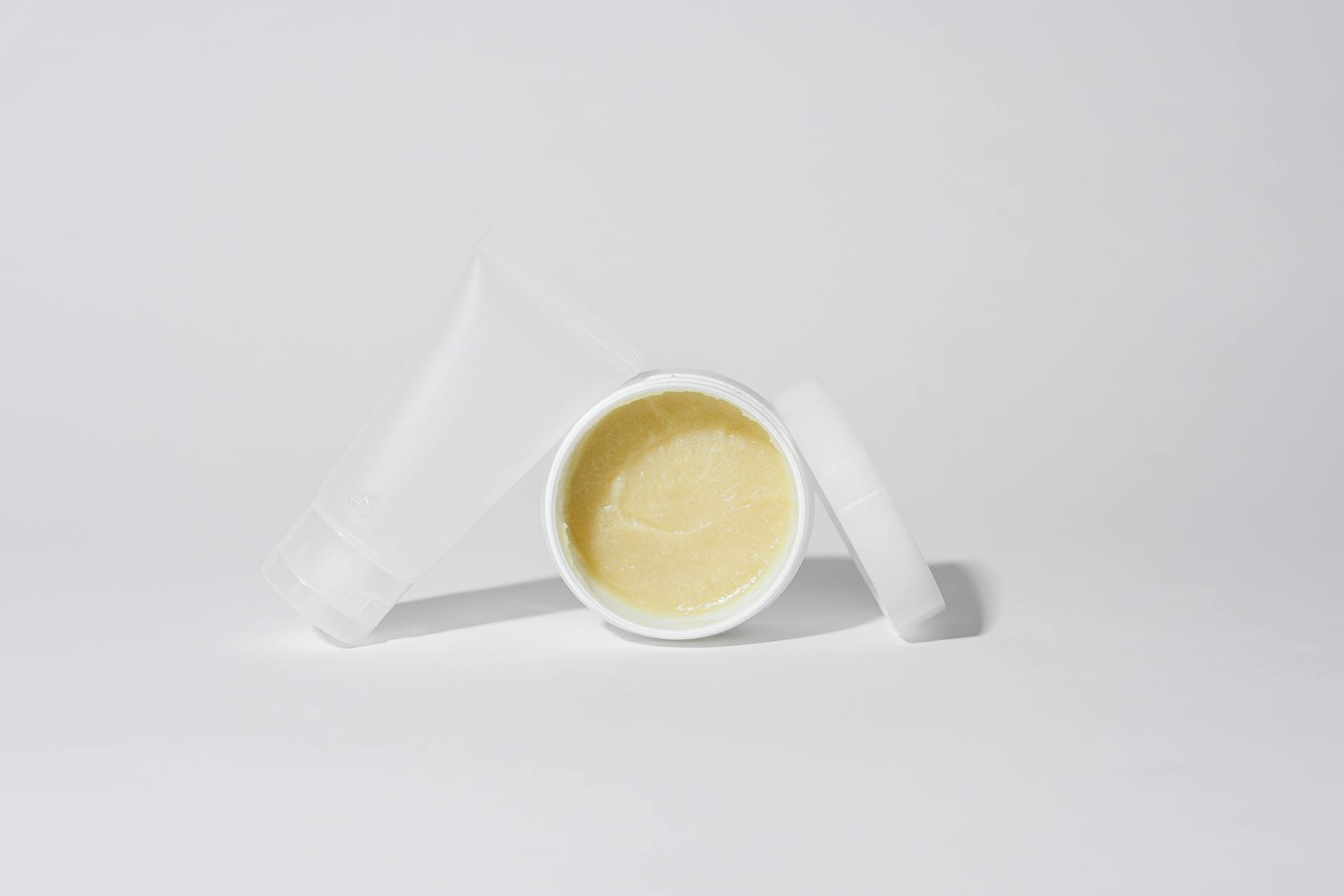 Studio shot of white plastic containers with yellow cream product on a white bac