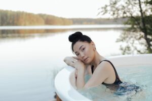 A woman enjoys a relaxing time in an outdoor hot tub by a serene lakeside settin