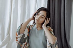 Asian woman in loungewear with headphones, eyes closed, enjoying music in a sere