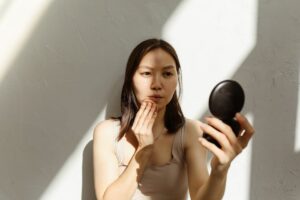 Young Asian woman applying makeup with a mirror in soft natural lighting indoors