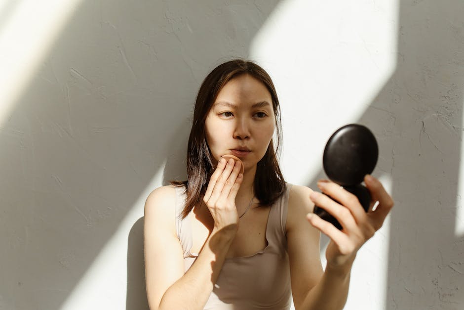 Young Asian woman applying makeup with a mirror in soft natural lighting indoors