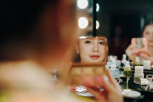 A woman applying makeup, captured in a mirror reflection surrounded by beauty pr