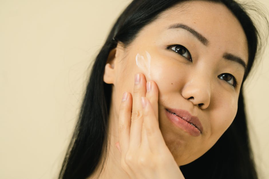 Woman with long black hair applying facial cream in studio. Focus on skincare an