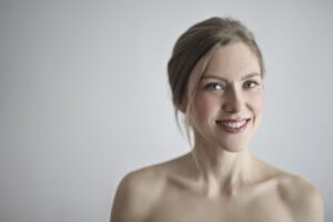 Close-up portrait of a smiling blonde woman against a gray background, embodying
