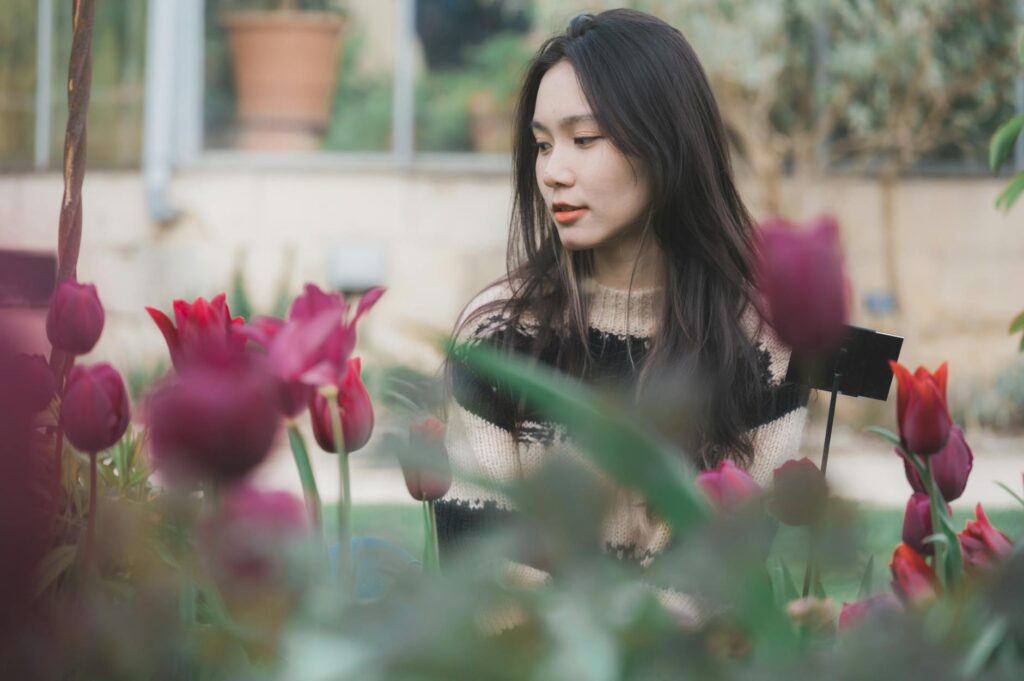 Asian woman in a knitted sweater amidst blooming tulips in outdoor garden.