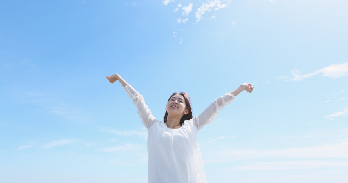 外で両手を広げて空を見上げる女性