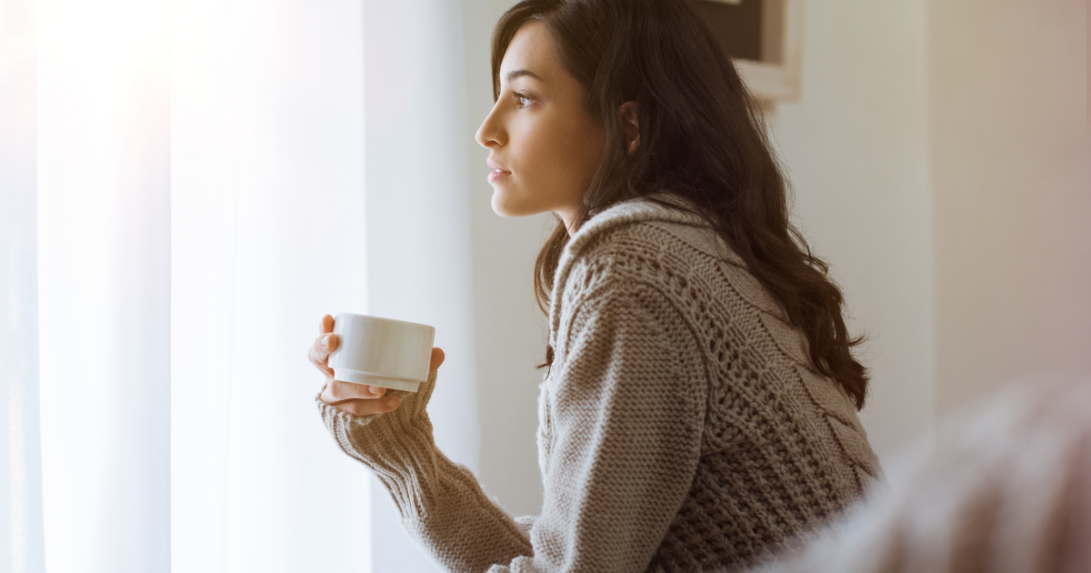 [mental] セーターでマグカップを持ち窓辺で物思いの女性（人物有）
