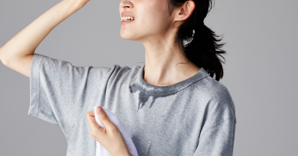 グレーTシャツで汗ばんだ脇を気にする笑顔の女性