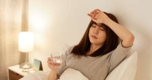 ベッドで水を飲み額に手を当てる女性