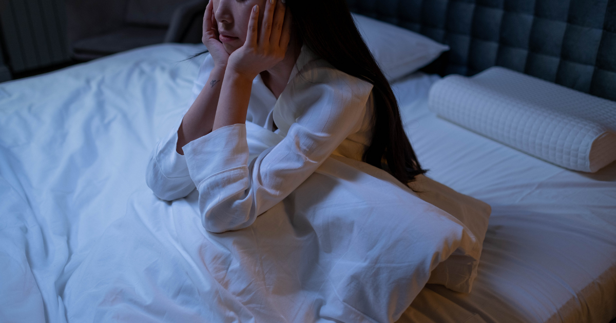 ベッドで頬杖をついて眠れない夜を過ごす女性