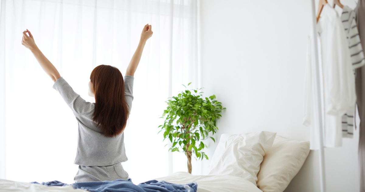 朝ベッドの上で伸びをする女性・目覚め