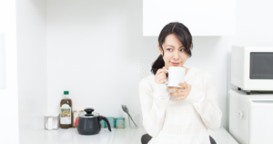 白いセーターを着た日本人女性がキッチンでマグカップを持って微笑む