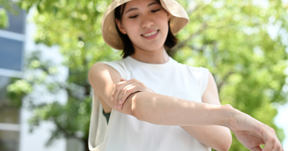 麦わら帽子をかぶった女性が屋外で腕に日焼け止めを塗る