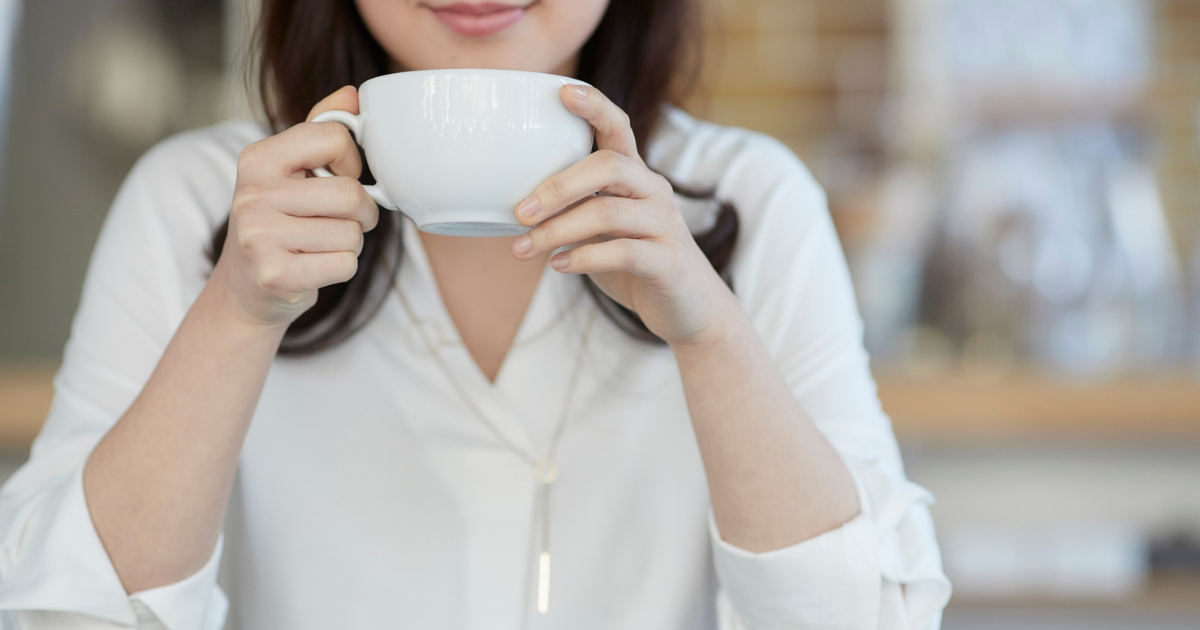 白いシャツの女性がカップを両手で持っている