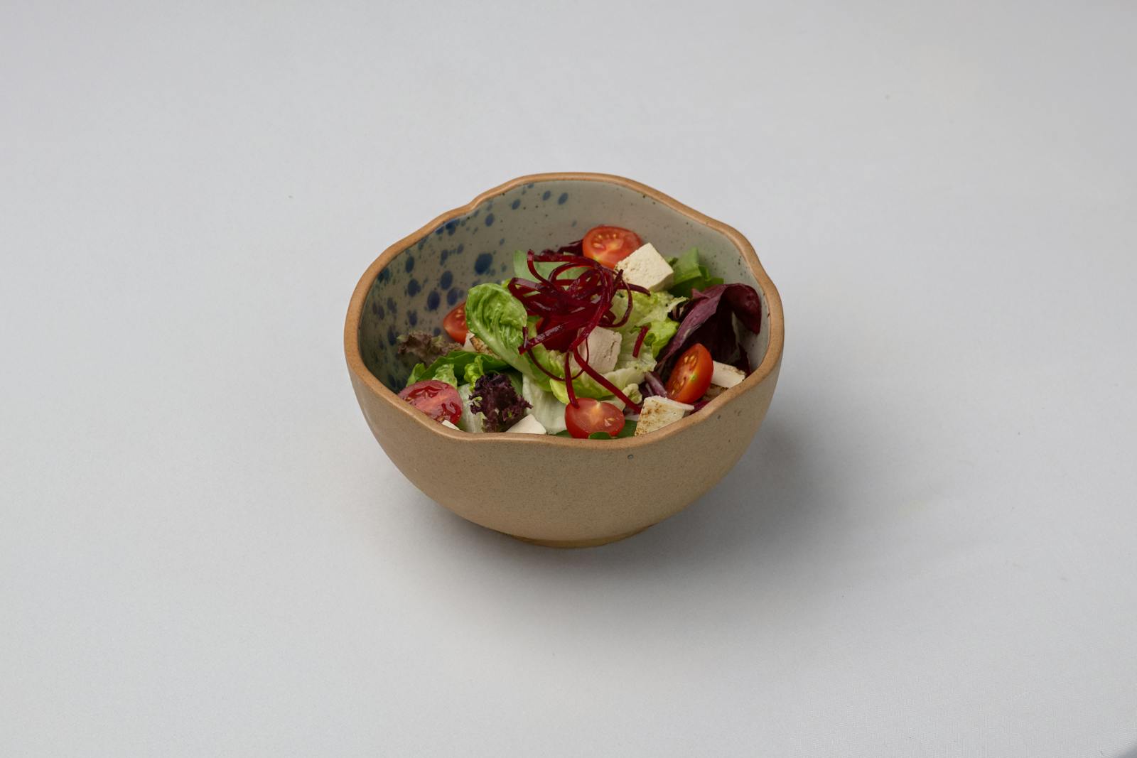 白い背景に置かれた、トマトと葉野菜のヘルシーなボウル