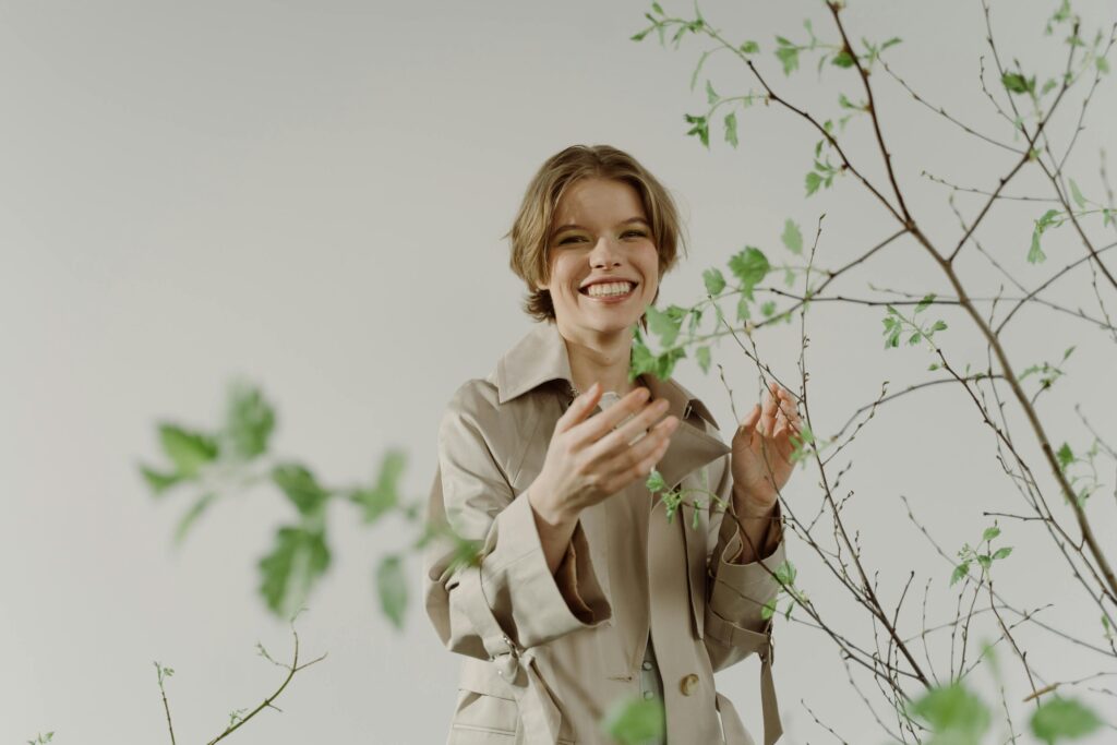 ベージュのコートを着て植物に触れる穏やかな女性・更年期ファッション