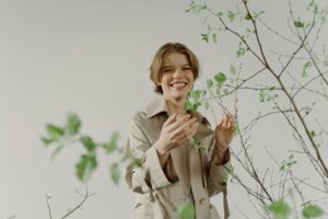 ベージュのコートを着て植物に触れる穏やかな女性・更年期ファッション