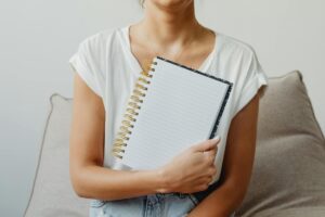 白いトップスの女性が空白のノートを抱える